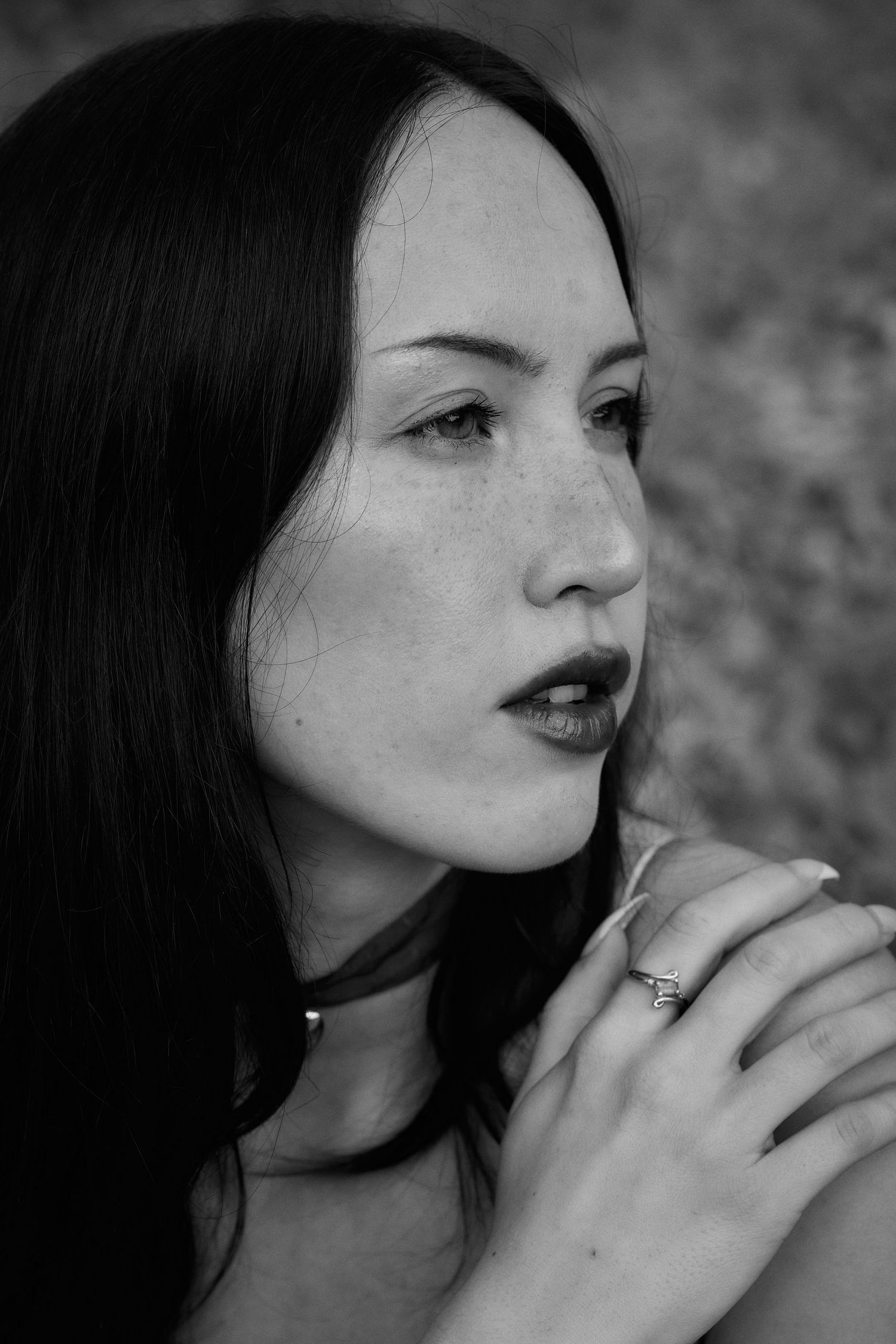 Black and white portrait of a woman with straight dark hair and bold lips in a contemplative pose against textured background.