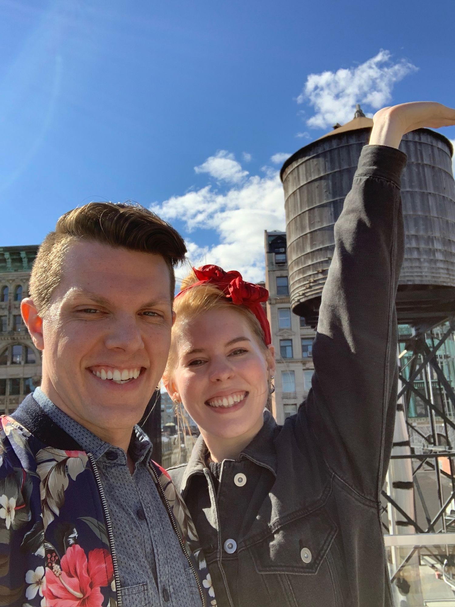Couple taking selfie in front of industrial silos on sunny day.