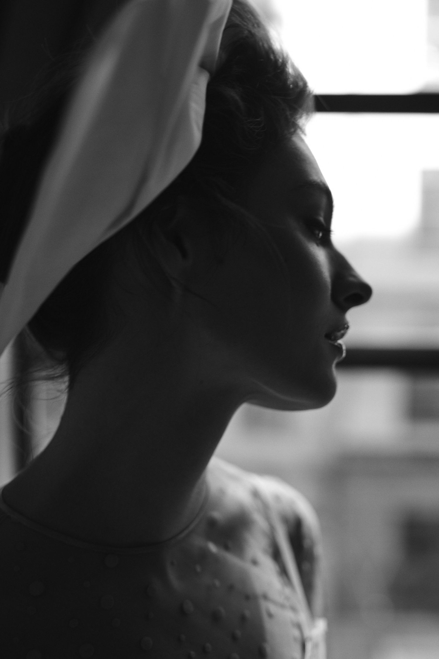 A silhouetted profile portrait of someone wearing a white head covering in dramatic lighting.