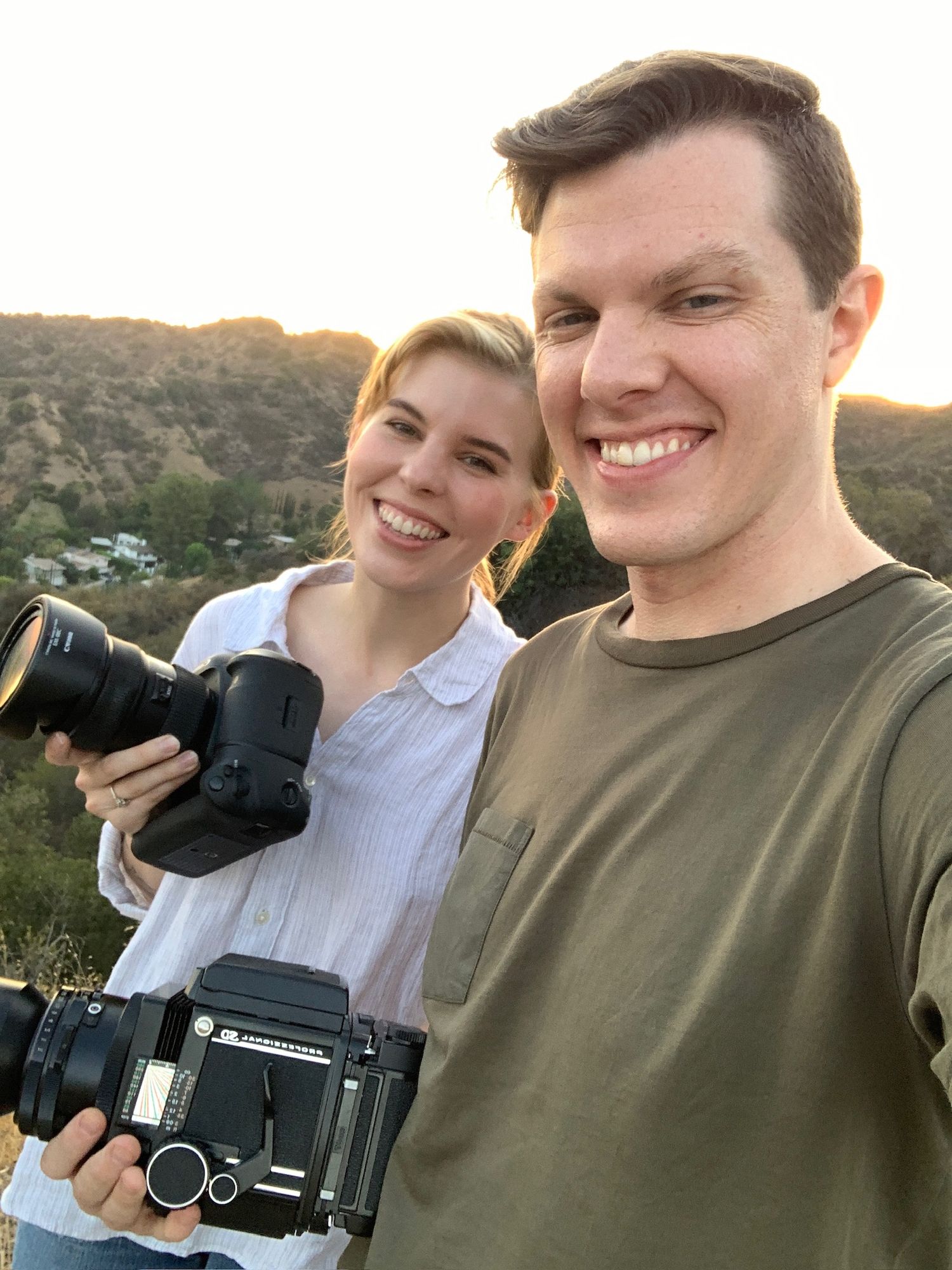 Adam Wamsley and Scout Wamsley, two photographers with professional film & digital cameras smile together at sunset in the mountains.