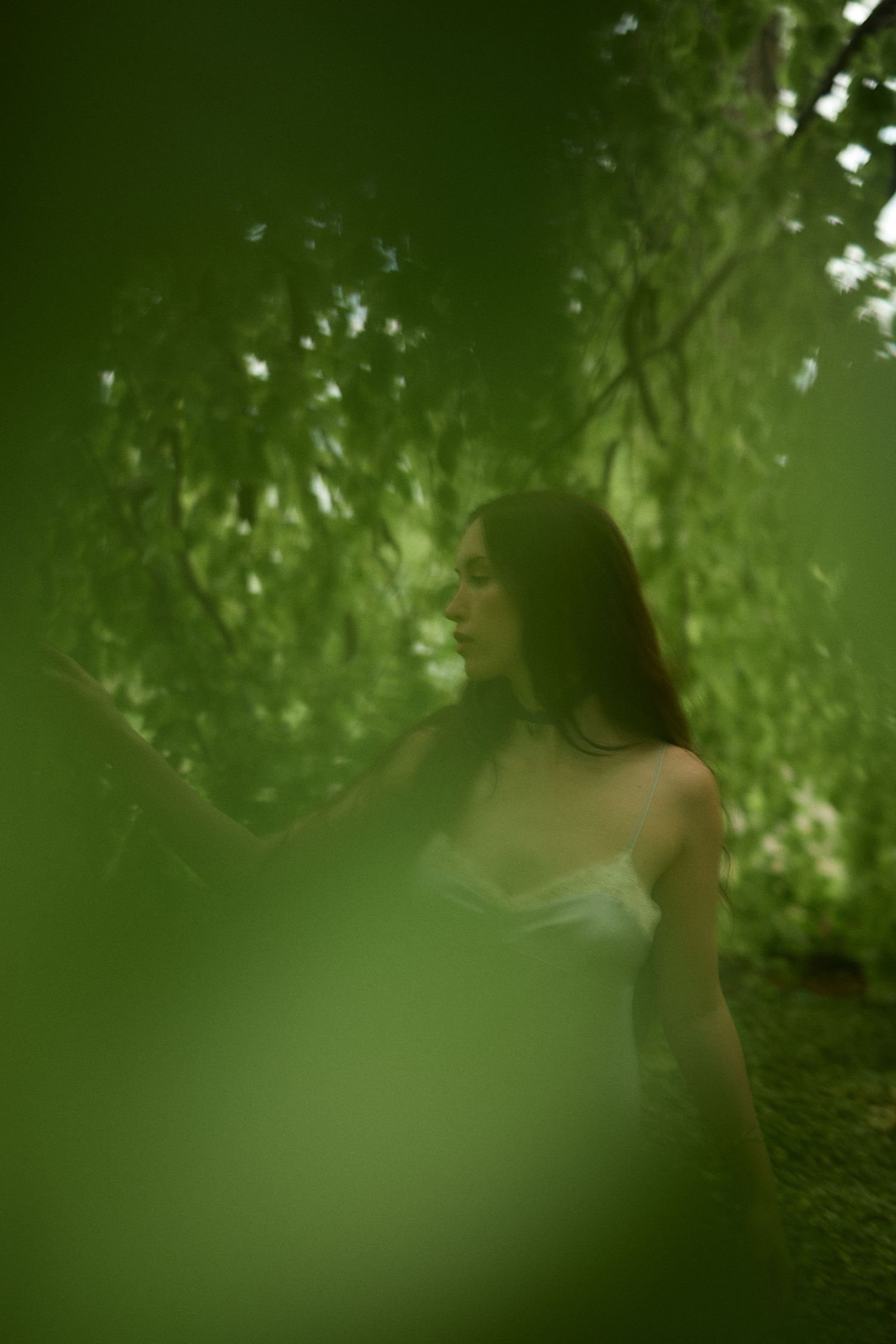 Dreamy forest portrait with soft green bokeh effect framing a figure in white against lush foliage.