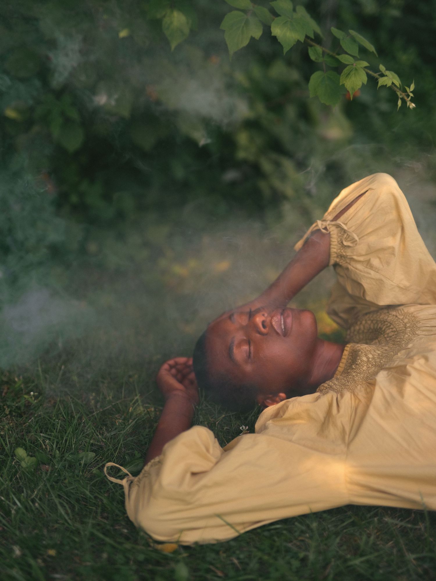 Person in yellow clothing lying peacefully on grass with misty atmosphere.