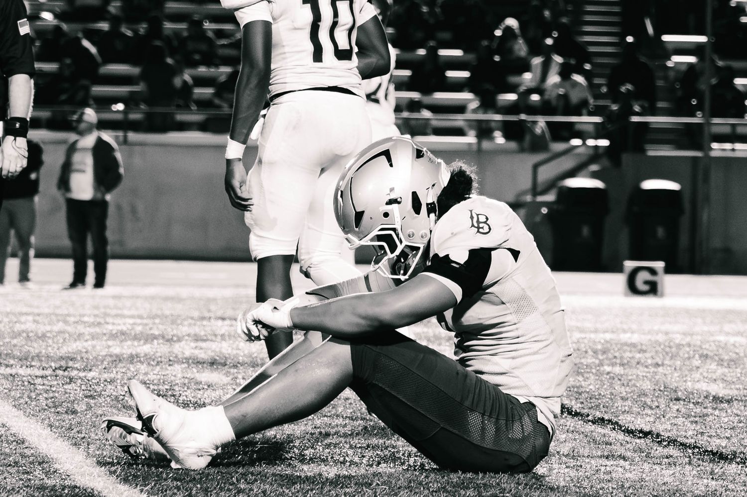 A black and white photo shows a football player sliding on the field during a game.