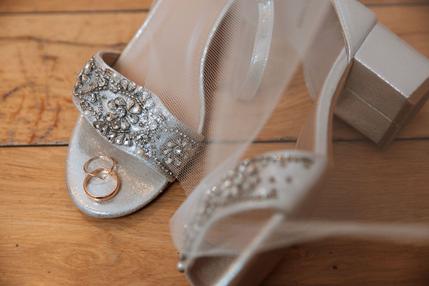 Wedding accessories and details including silver shoes and rings arranged on rustic wooden surface.