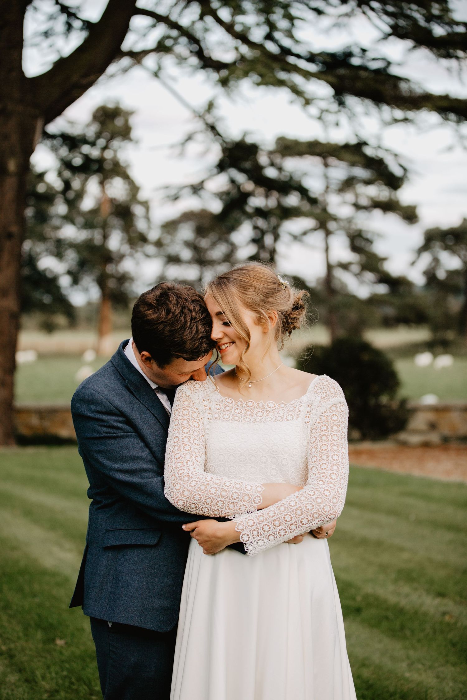 A romantic and candid wedding moment between wedding couple captured on a grassy Welsh hillside with evergreen trees in the background.