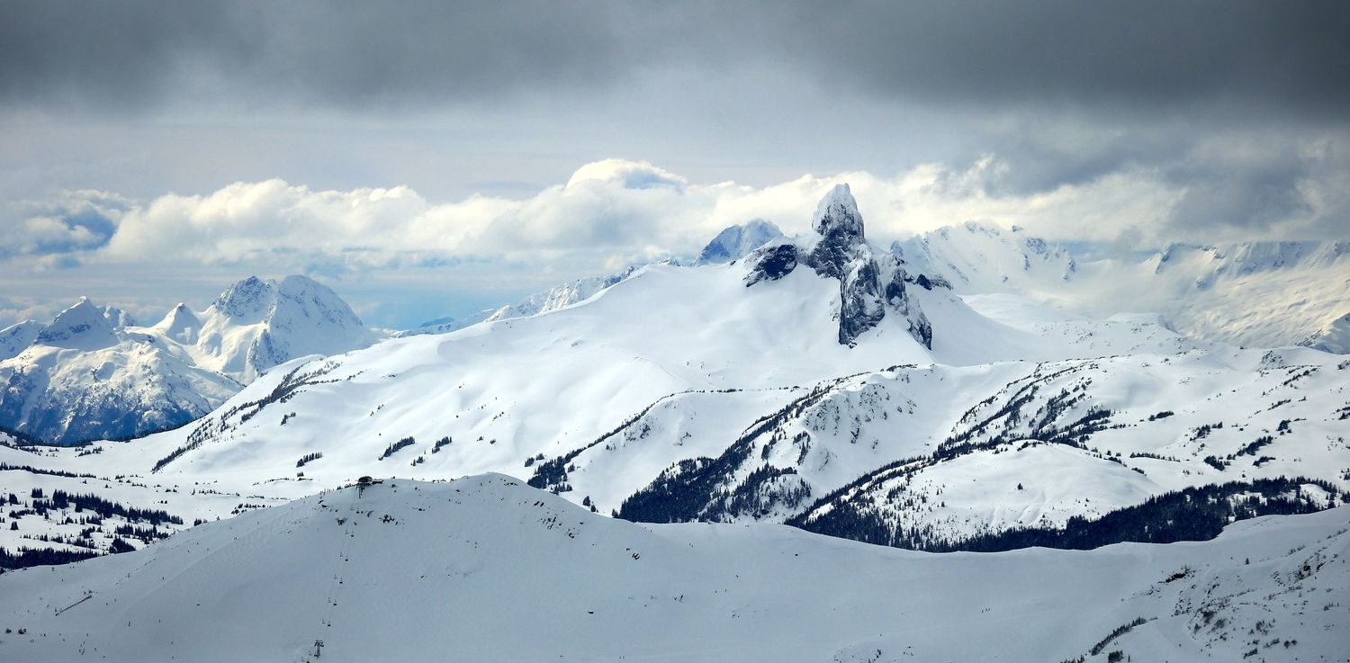 Snow-covered mountain peaks rise dramatically against moody clouds in a winter alpine landscape.
