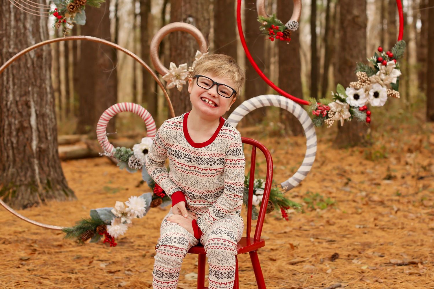 Holiday photo session in woods with red chair and festive winter decorations.