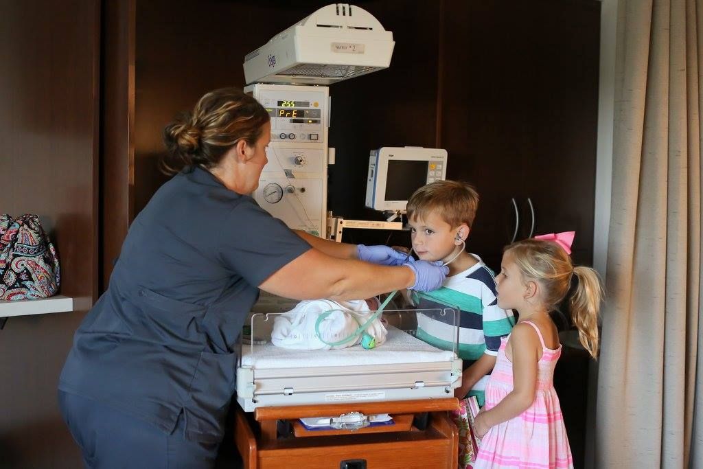 Family members visiting and interacting with newborn in hospital room.