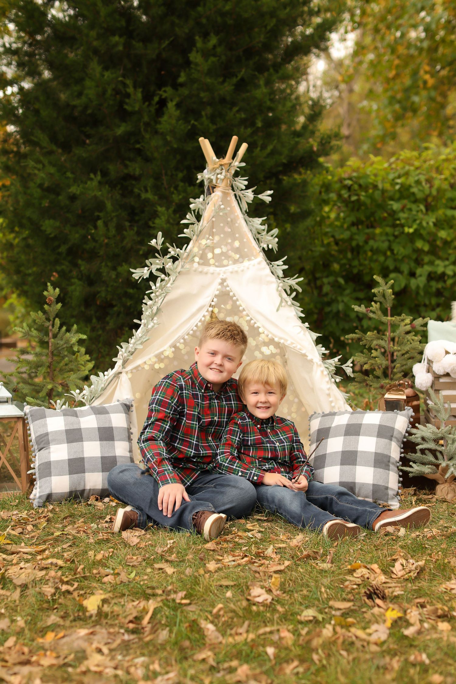 Outdoor autumn photo setup with white teepee tent and buffalo plaid pillows on fallen leaves.