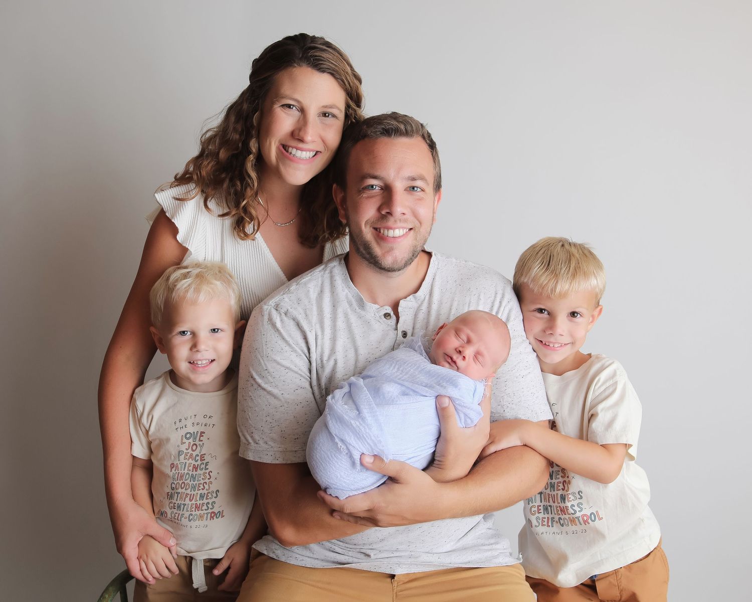 Family portrait with two young children and newborn baby against white background.