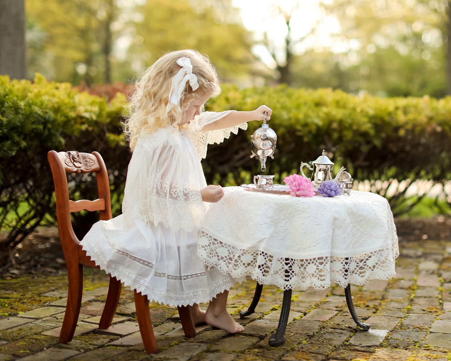 Elegant tea party setup with lace tablecloths and vintage chairs in an outdoor garden setting.