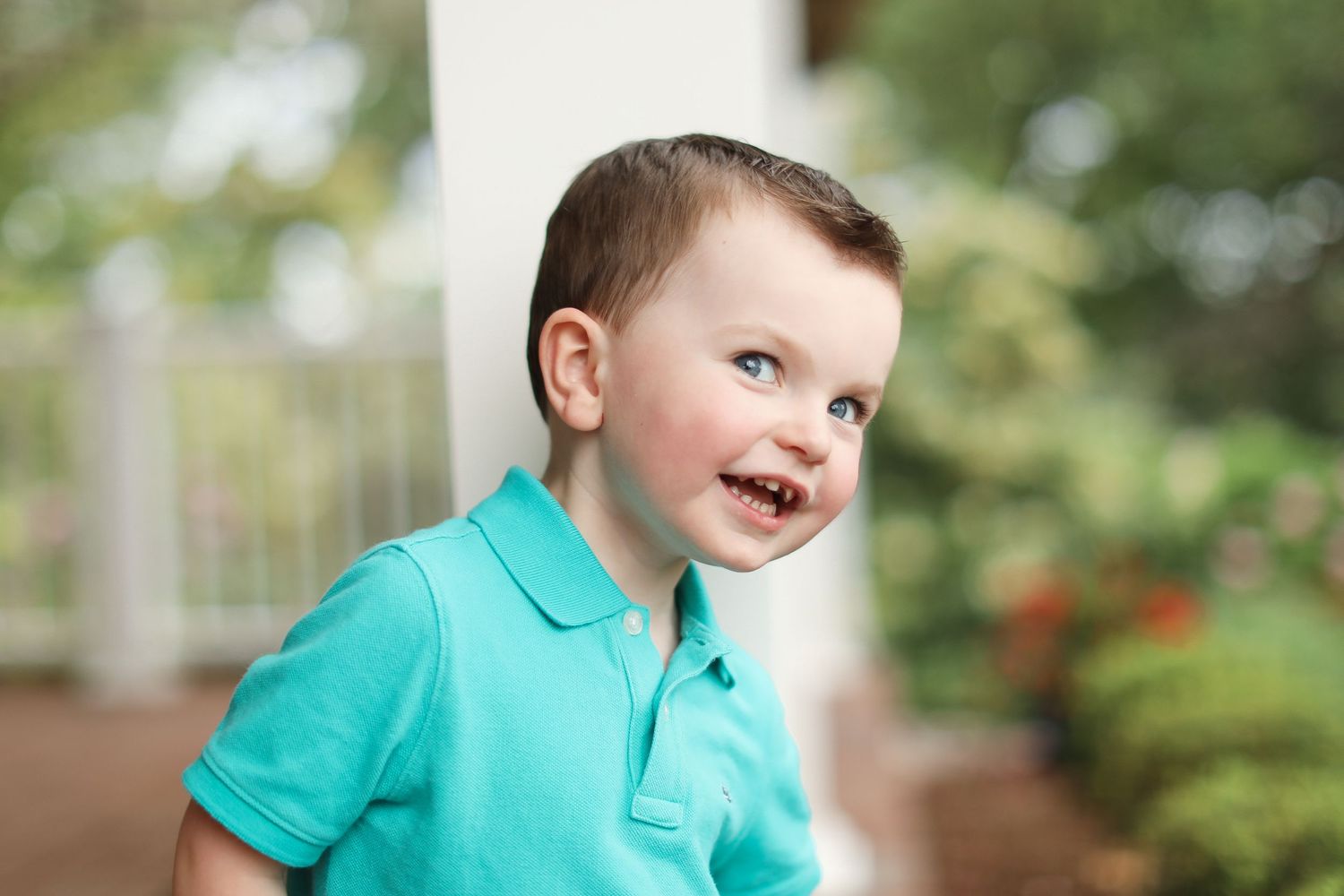 Child wearing turquoise polo shirt smiling against blurred outdoor background.