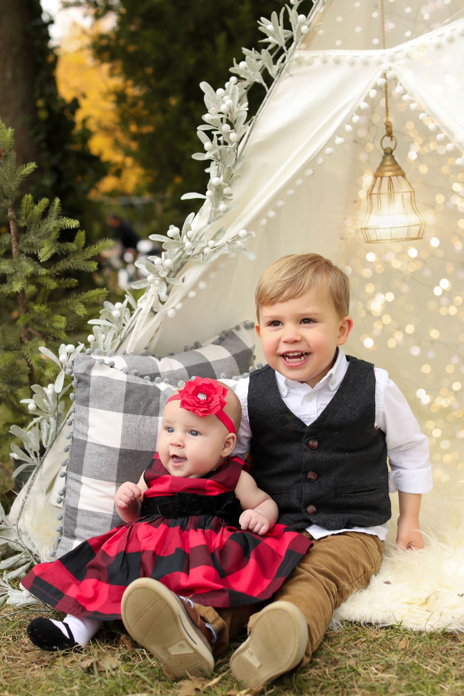 Holiday photo setup with white teepee tent, buffalo plaid pillows, and festive red and white decor.