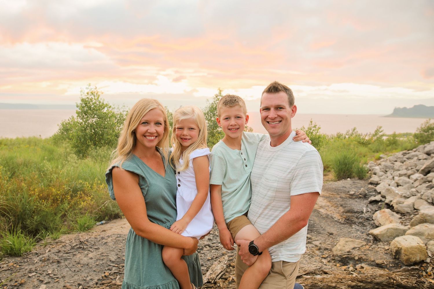 Family portrait on rocky shoreline during sunset with coordinated casual outfits.