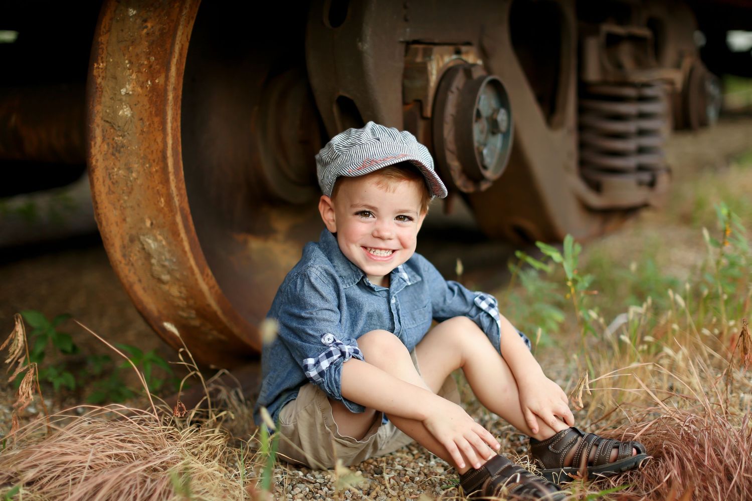 Child sitting by rustic farm equipment wearing denim and baseball cap.