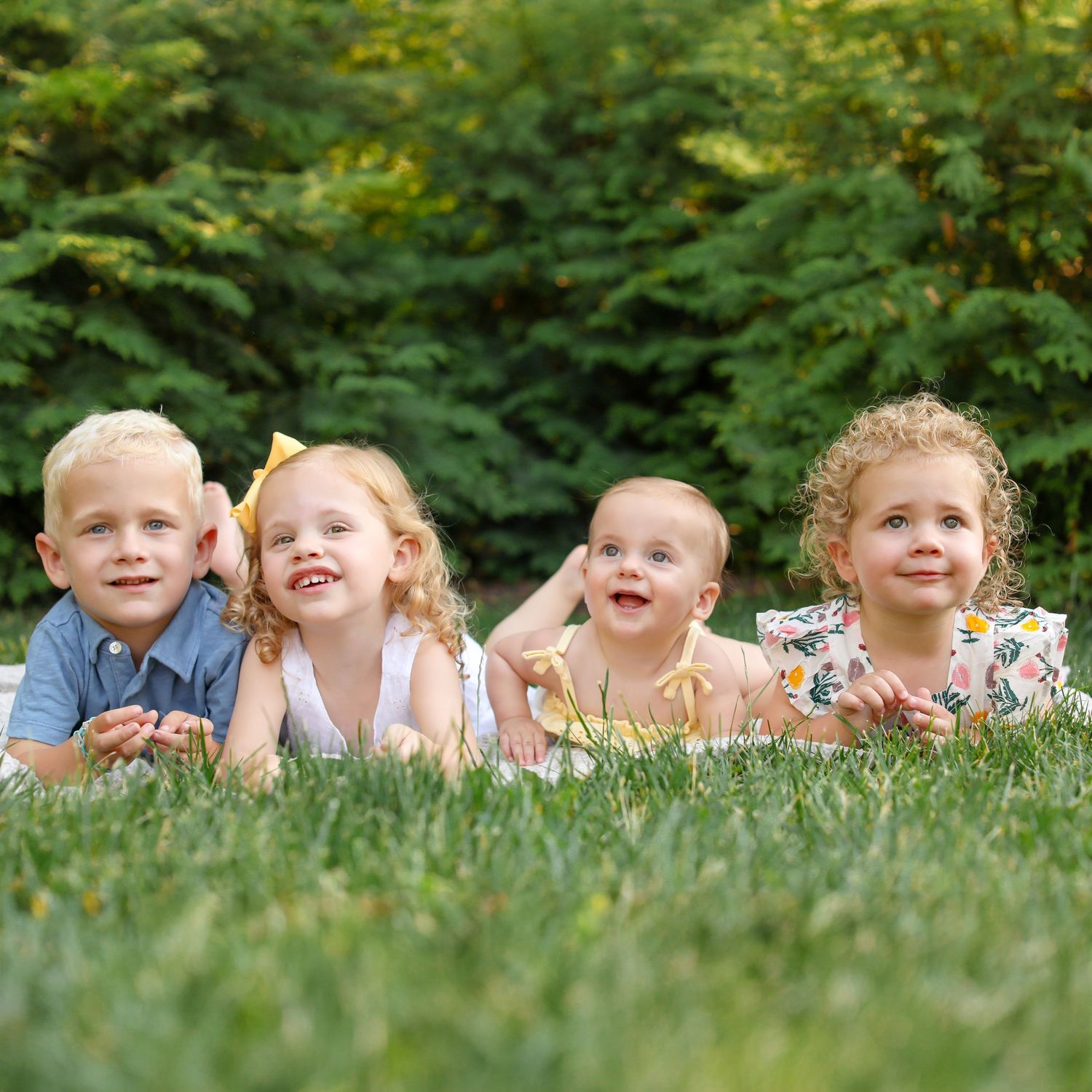 Children laying in a row on green grass during a summer photoshoot.