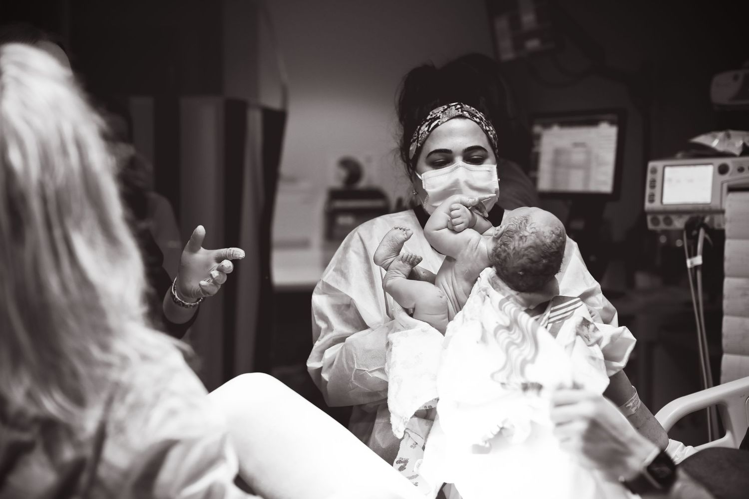 Medical staff in protective gear caring for newborn in hospital delivery room setting.