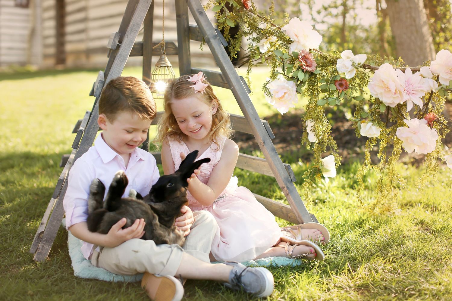 Family playing and cuddling in a sunlit garden setting with blooming flowers in the background.