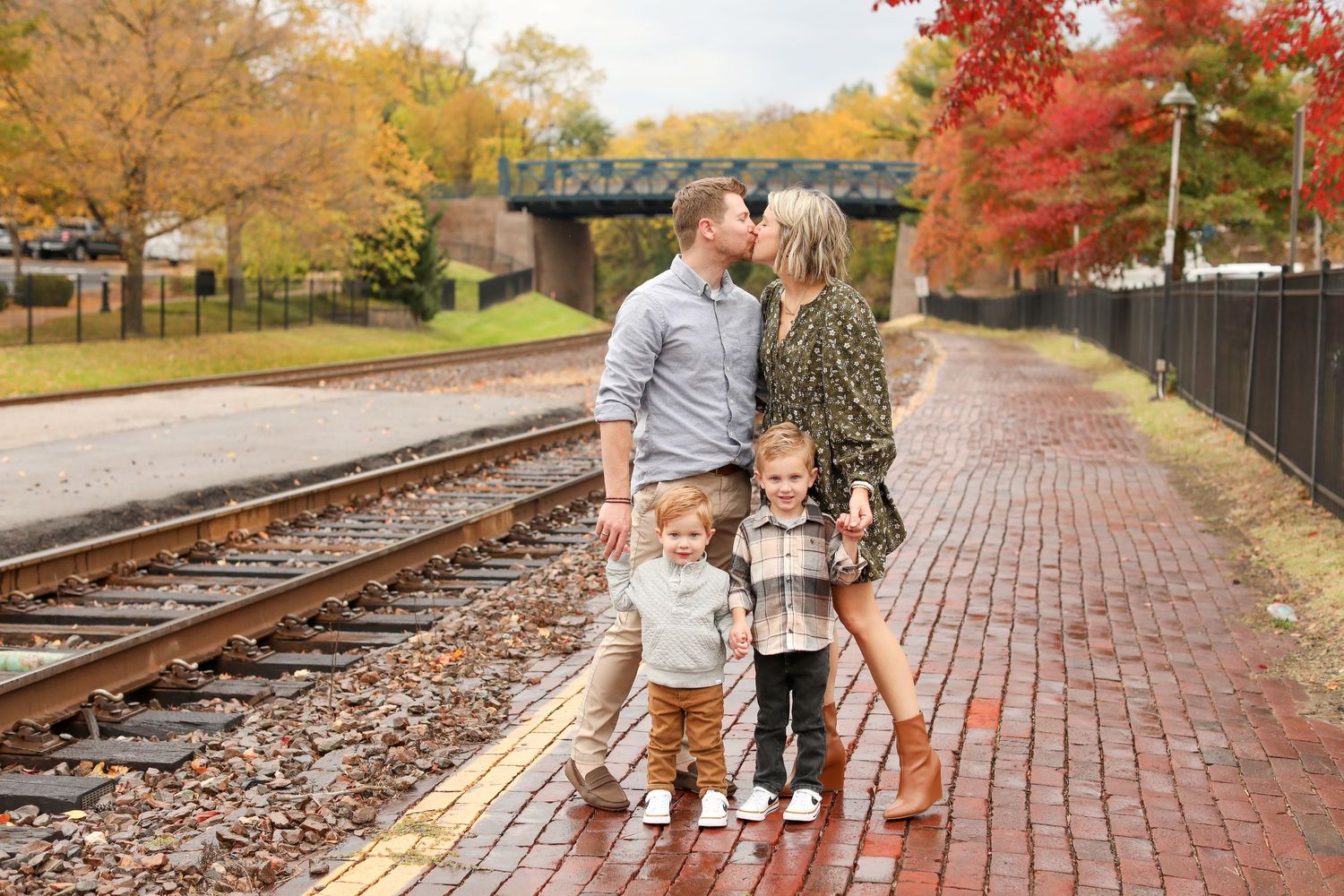 A group stands near train tracks in autumn with colorful fall foliage in the background.
