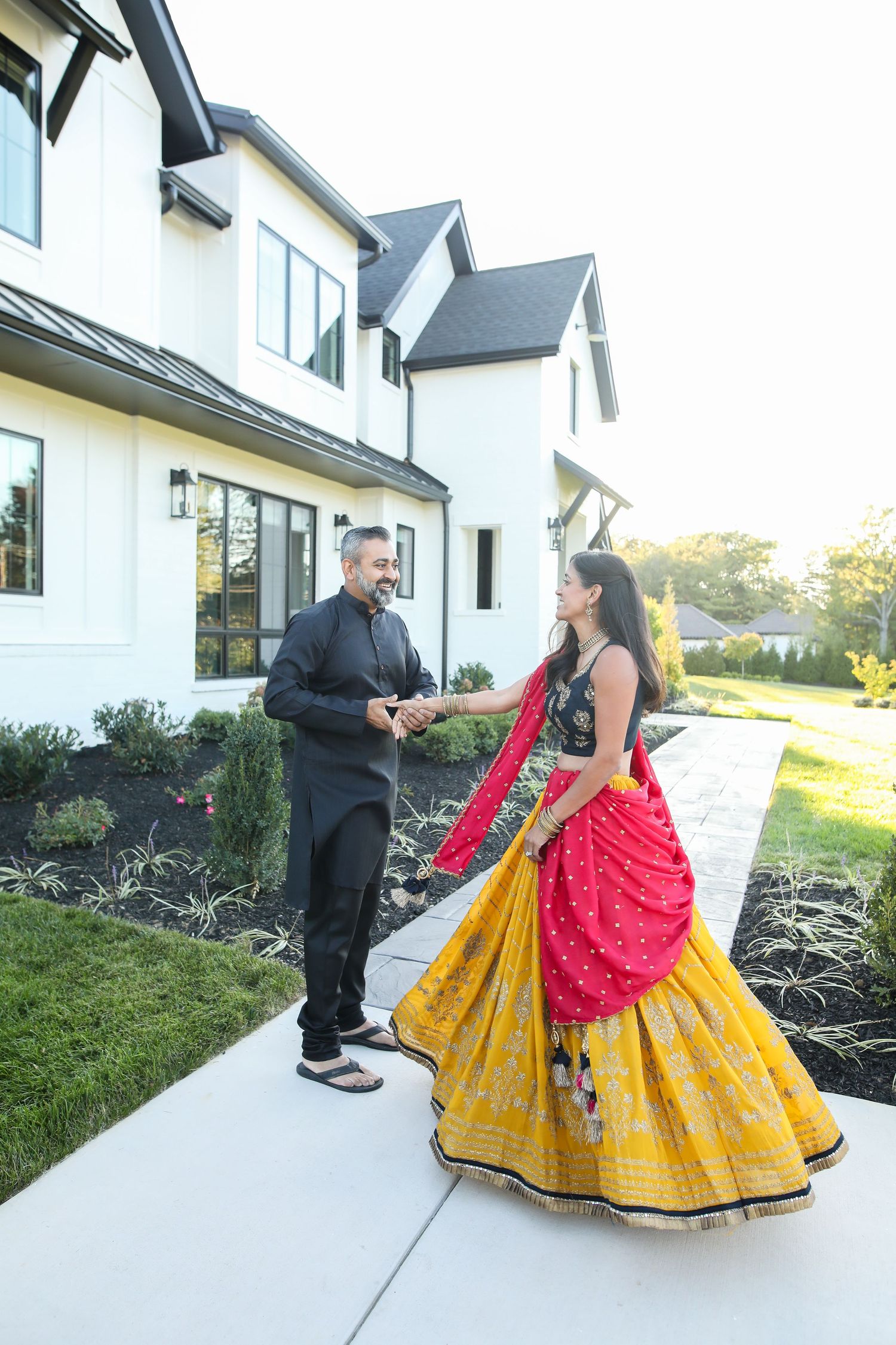 Two people dancing together in front of a modern white farmhouse on a sunny day.