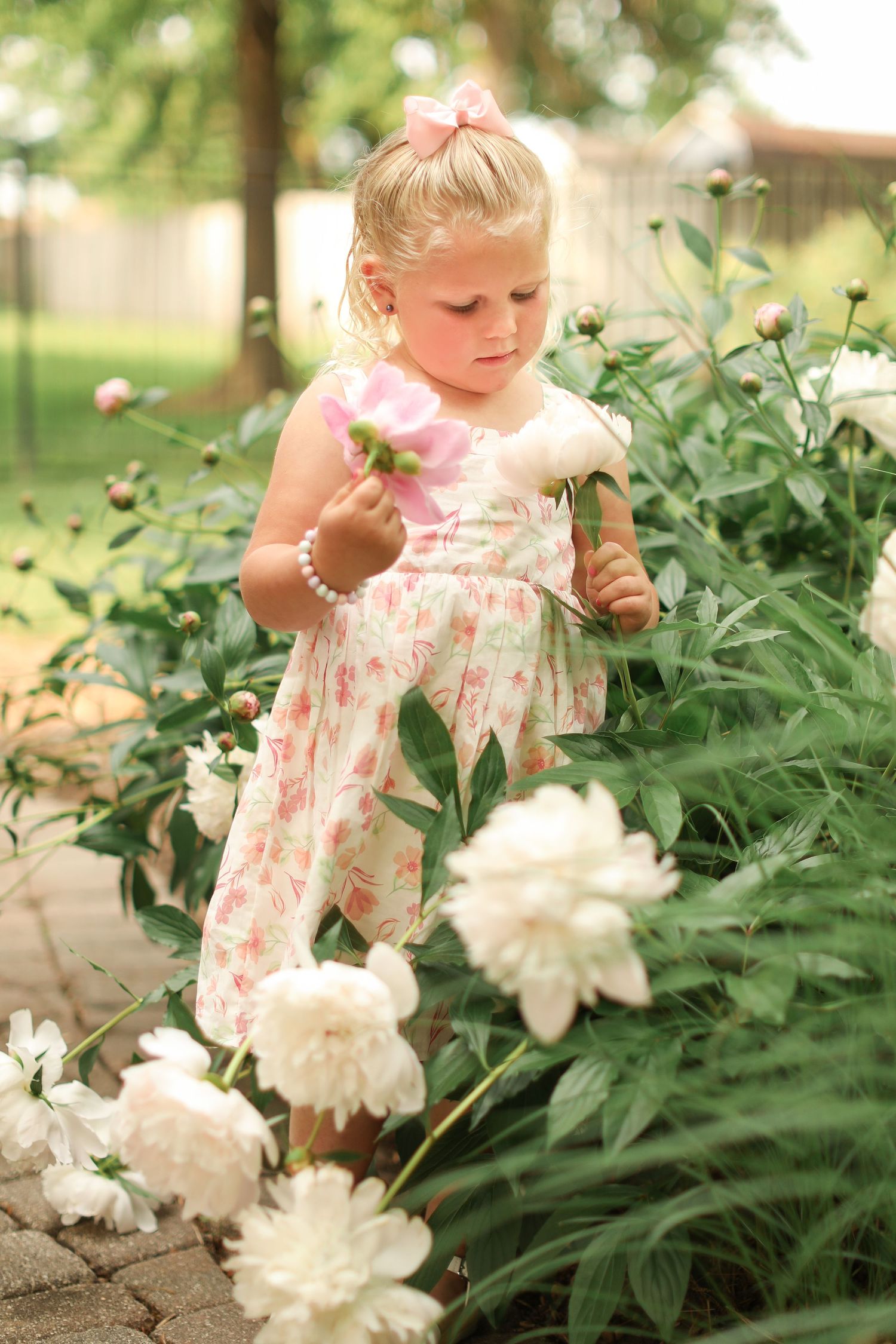 Child in floral dress exploring white peonies in garden setting.