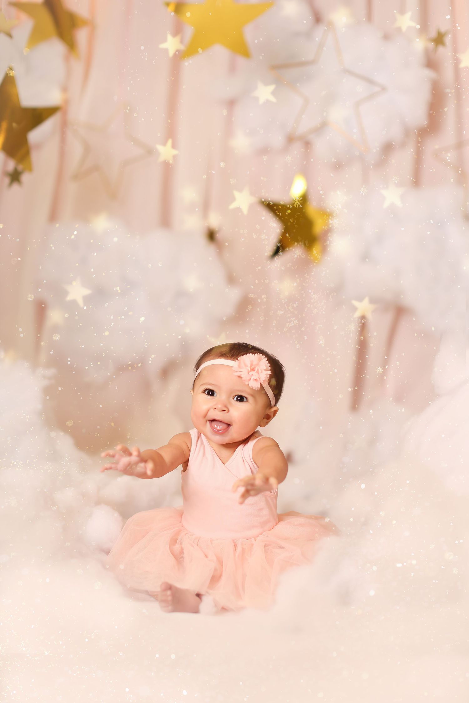 Baby in pink tutu dress surrounded by floating gold stars and white clouds in dreamy setting.