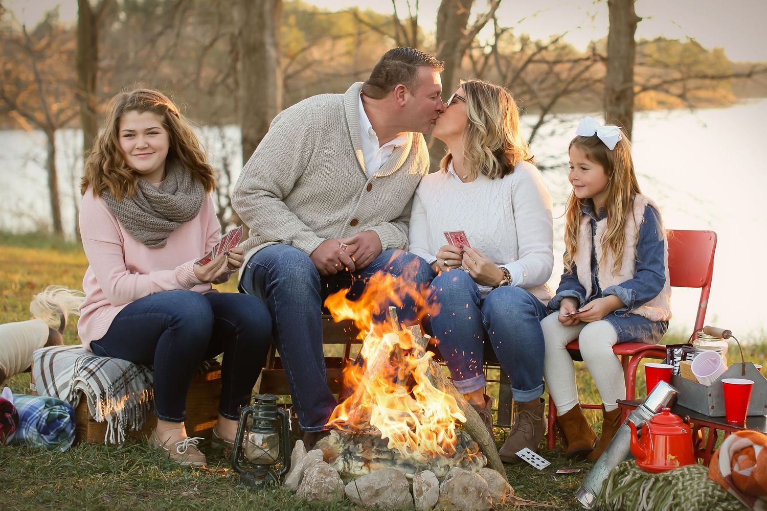 Group gathered around cozy campfire by lake during autumn sunset.