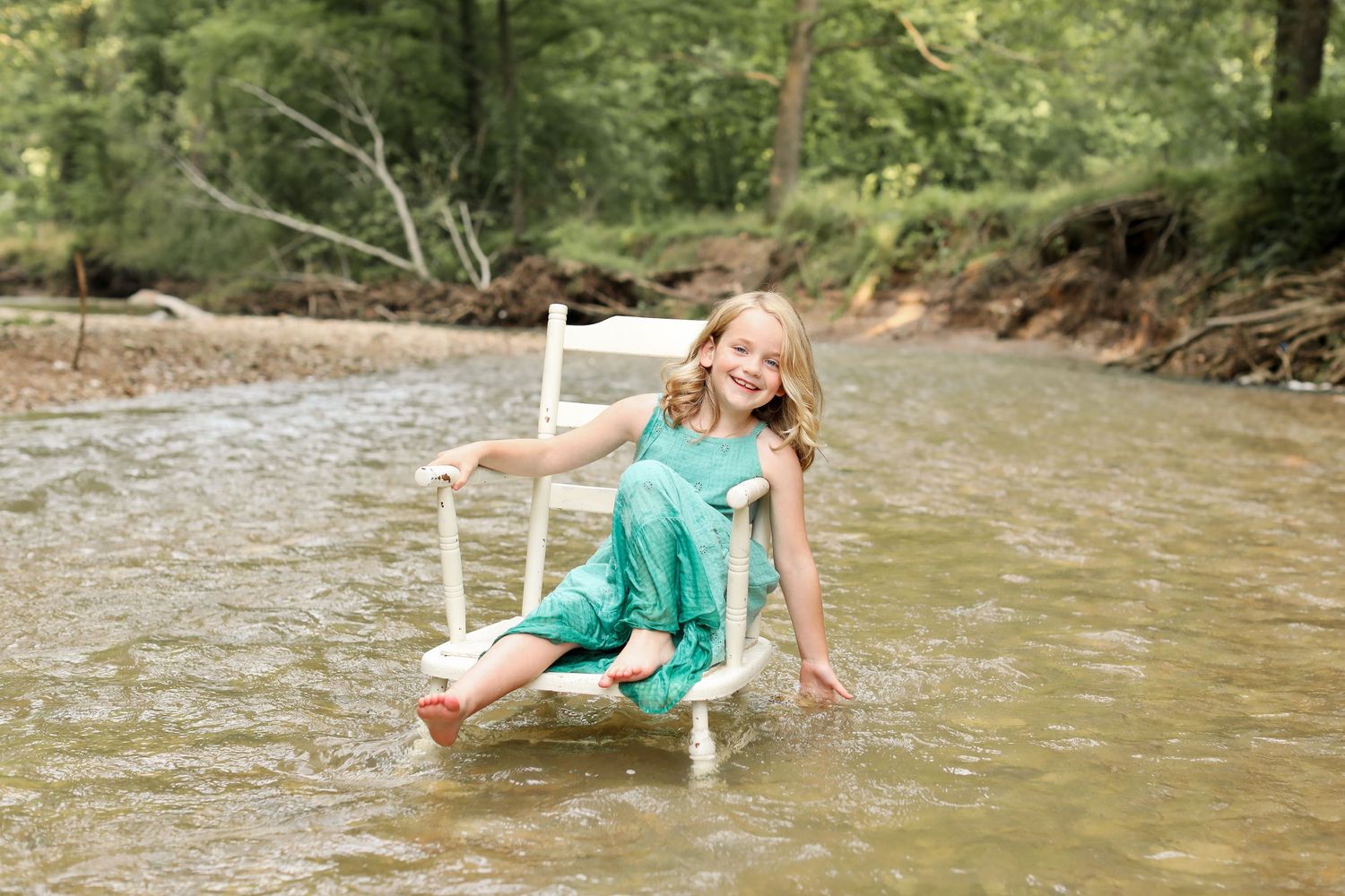 Person in turquoise dress playing in shallow creek water on sunny day.