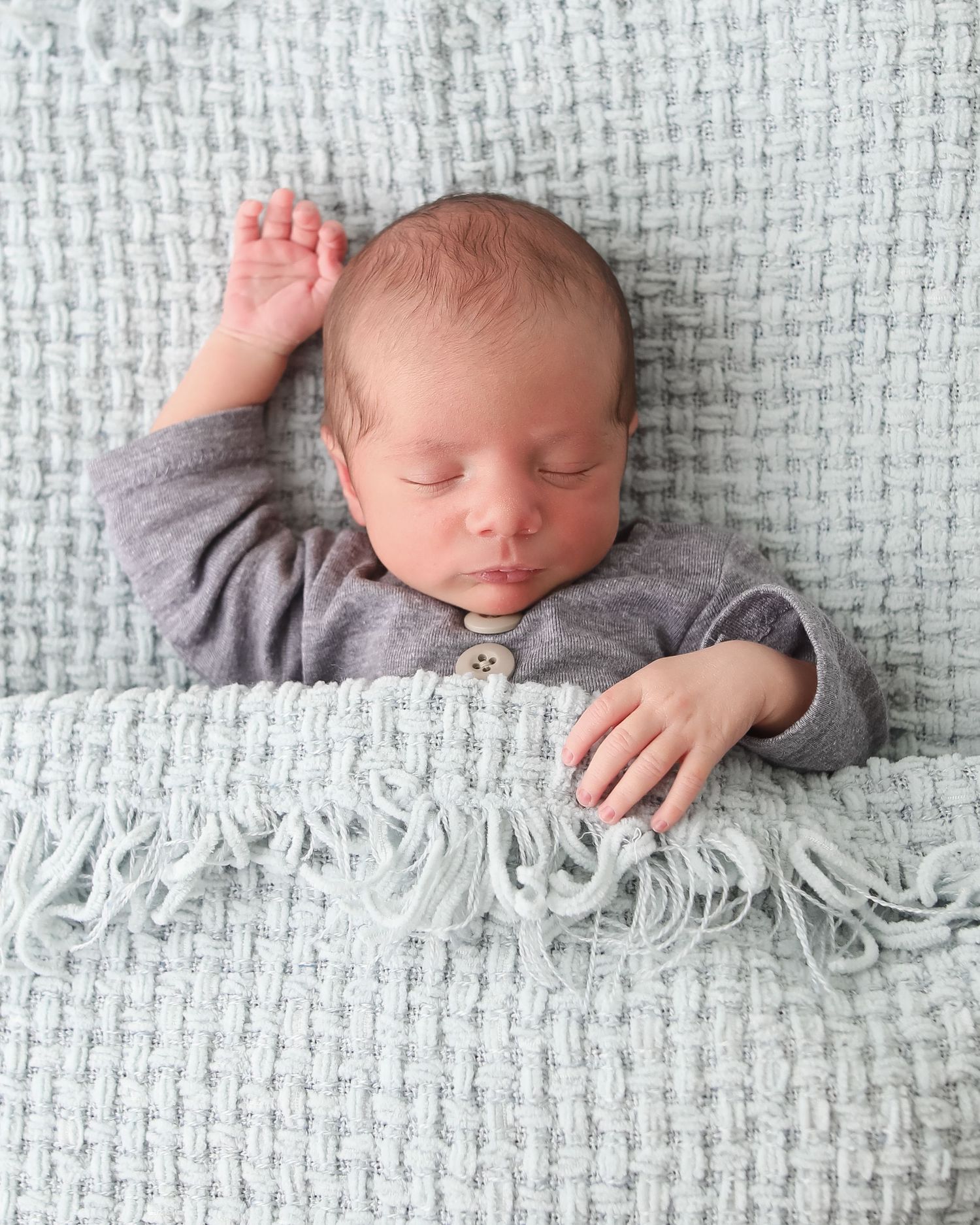 Baby resting on textured white blanket during newborn portrait session.