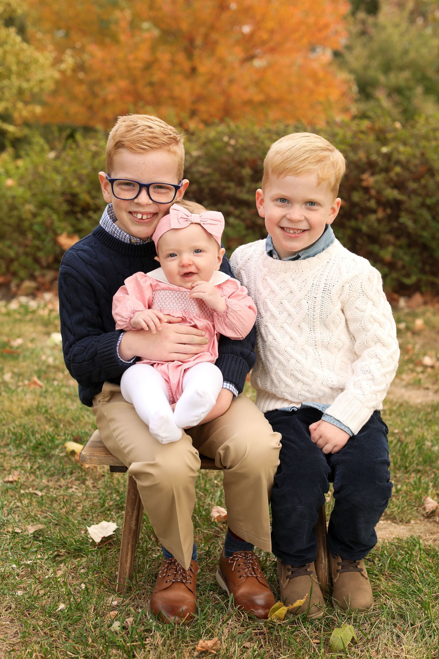 Children sitting together on bench during autumn outdoor photo session.