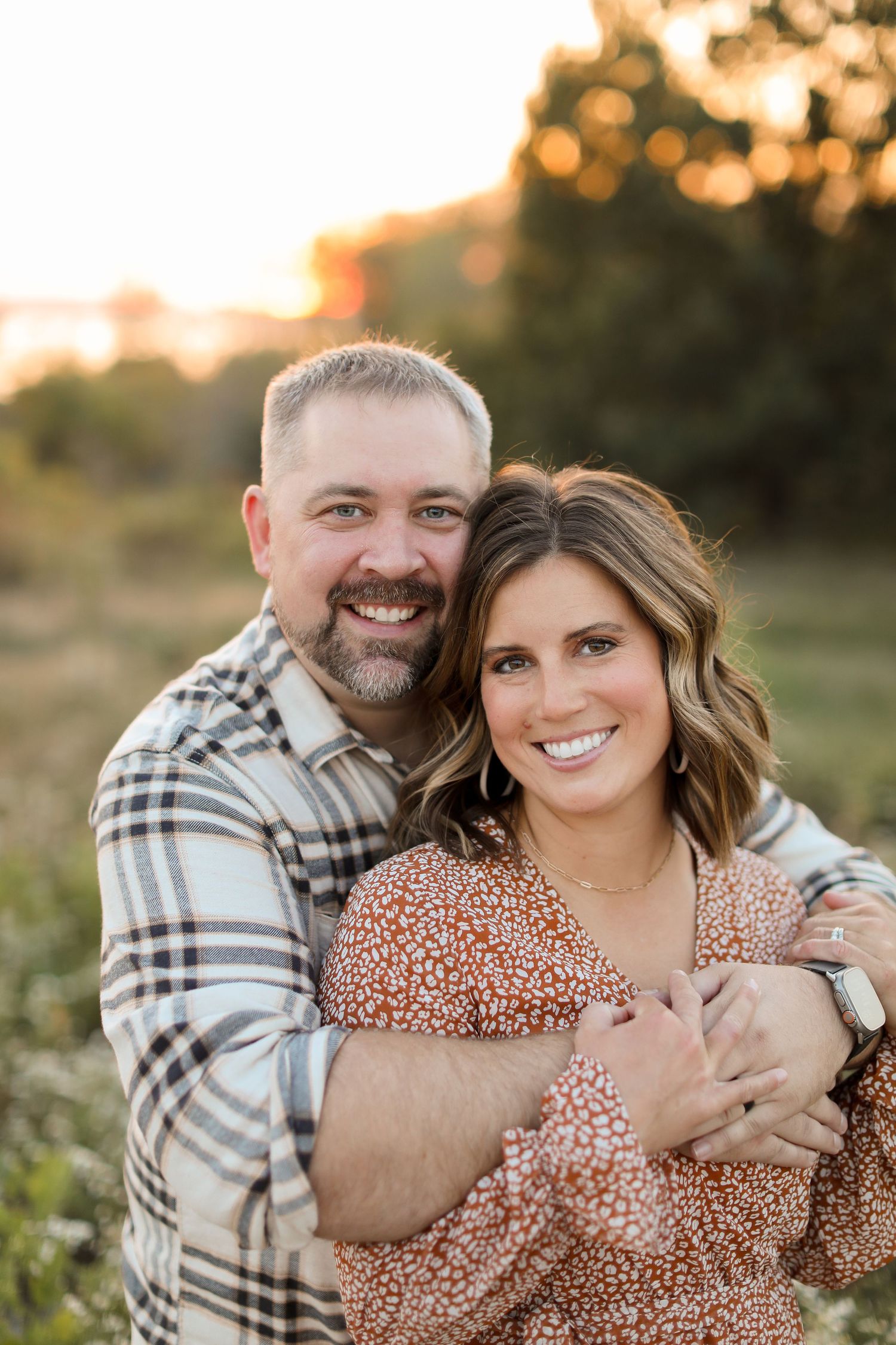 Couple embracing outdoors during golden hour sunset in casual clothing.