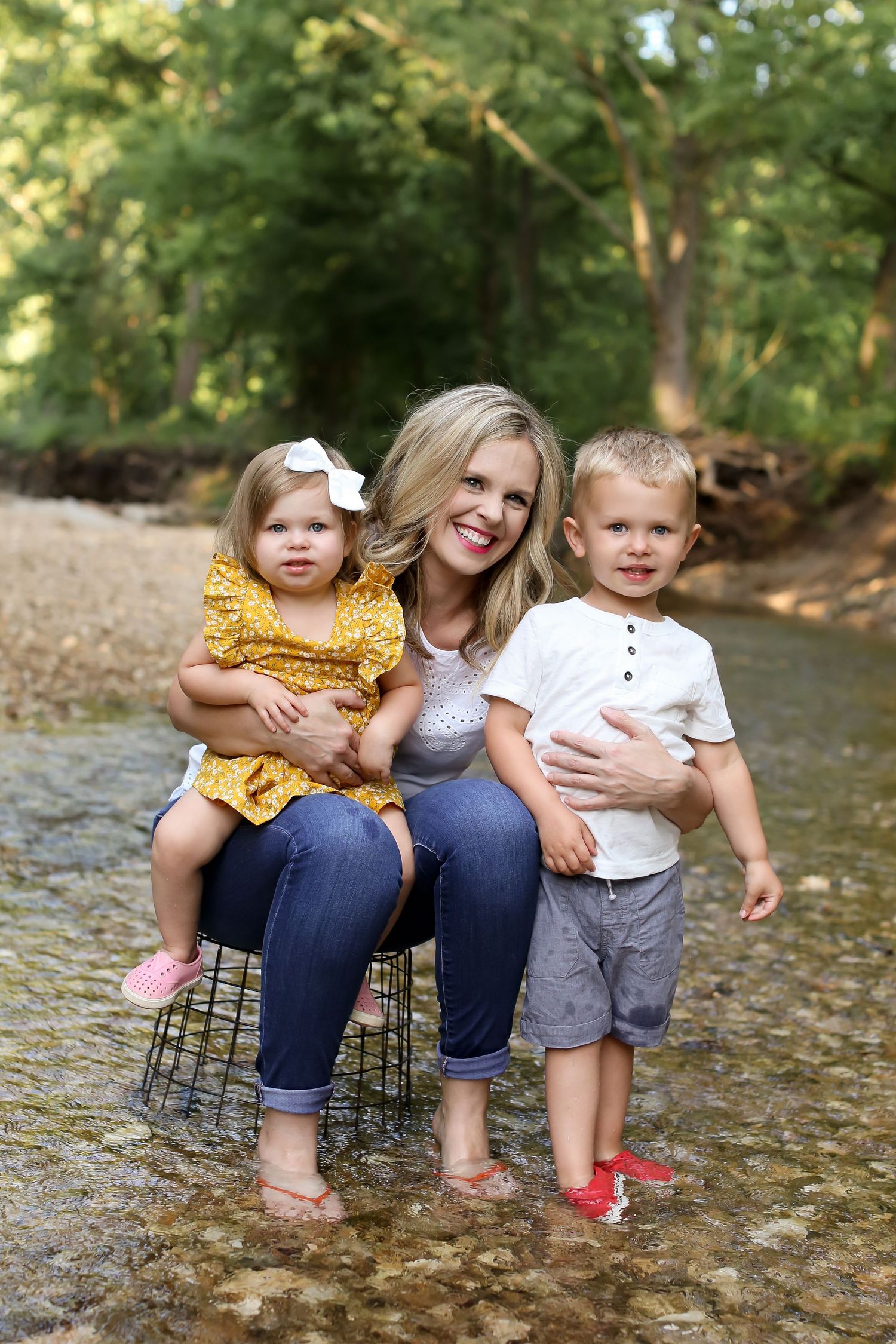 Family portrait sitting together in a creek bed surrounded by green trees.