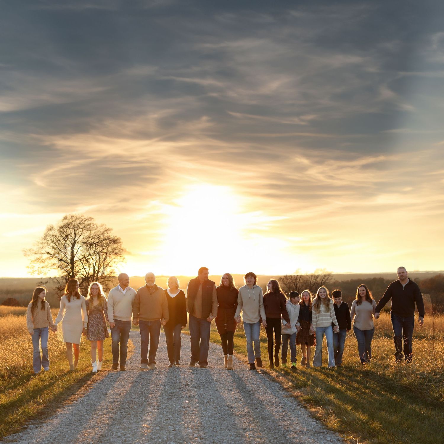 Large group silhouetted against dramatic sunset sky on rural path.
