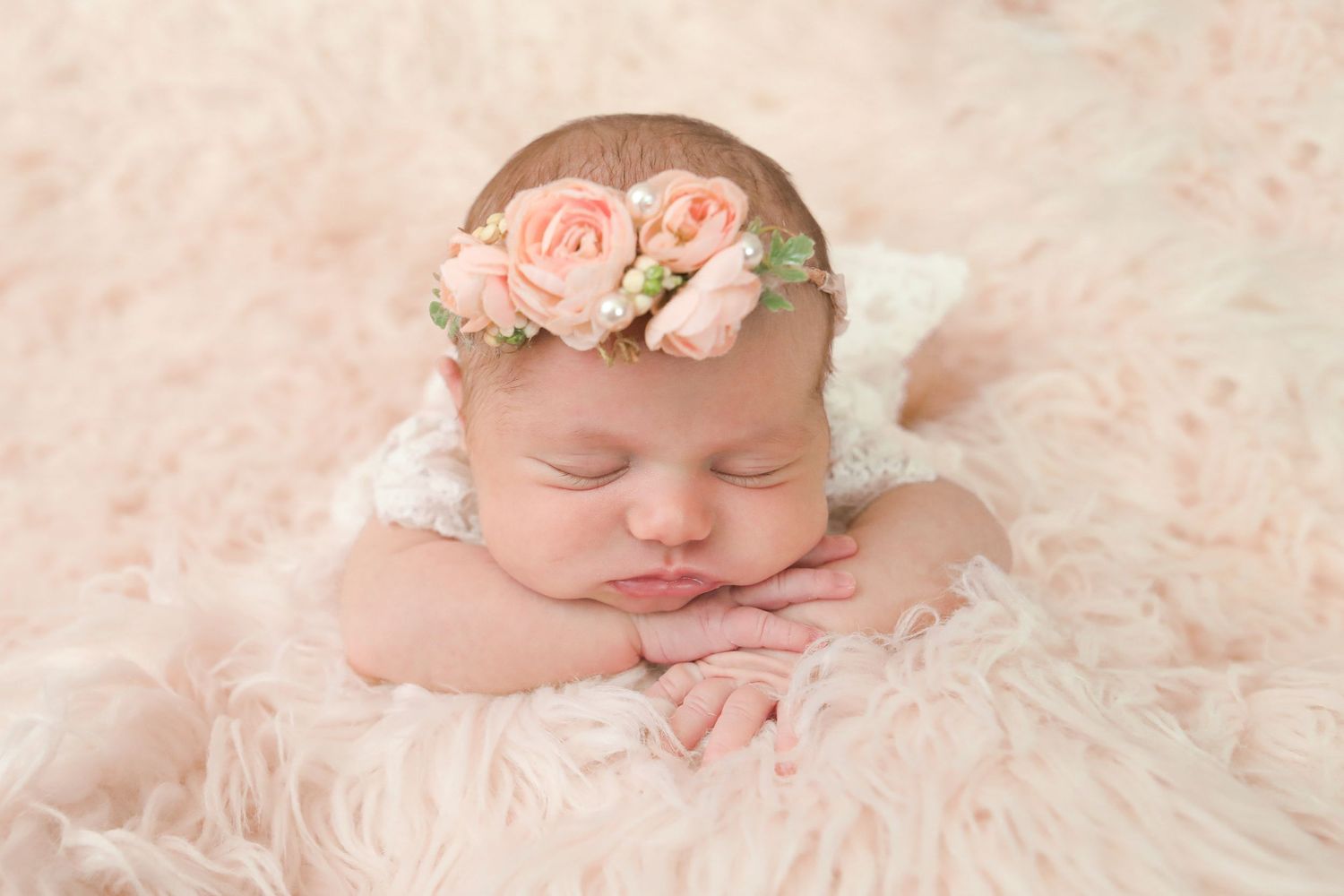 Sleeping baby wearing delicate floral crown on pink furry backdrop.