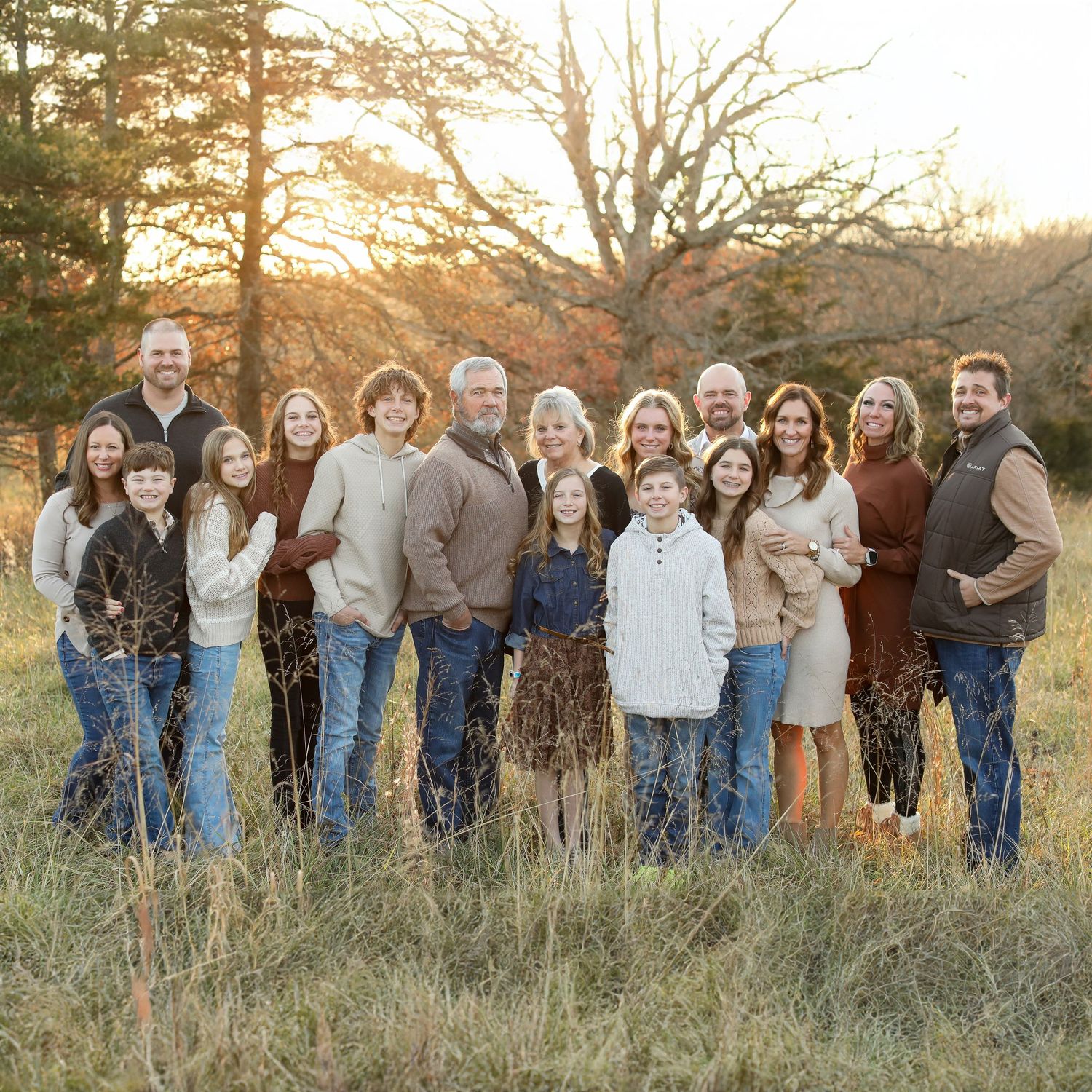 Extended family group portrait in golden field at sunset wearing coordinated denim and neutral colors.