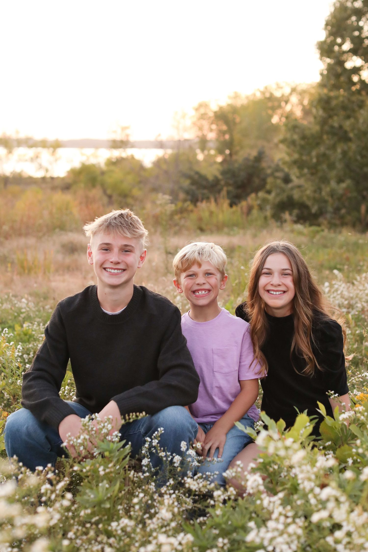 Three people sit together in a wildflower field at sunset.