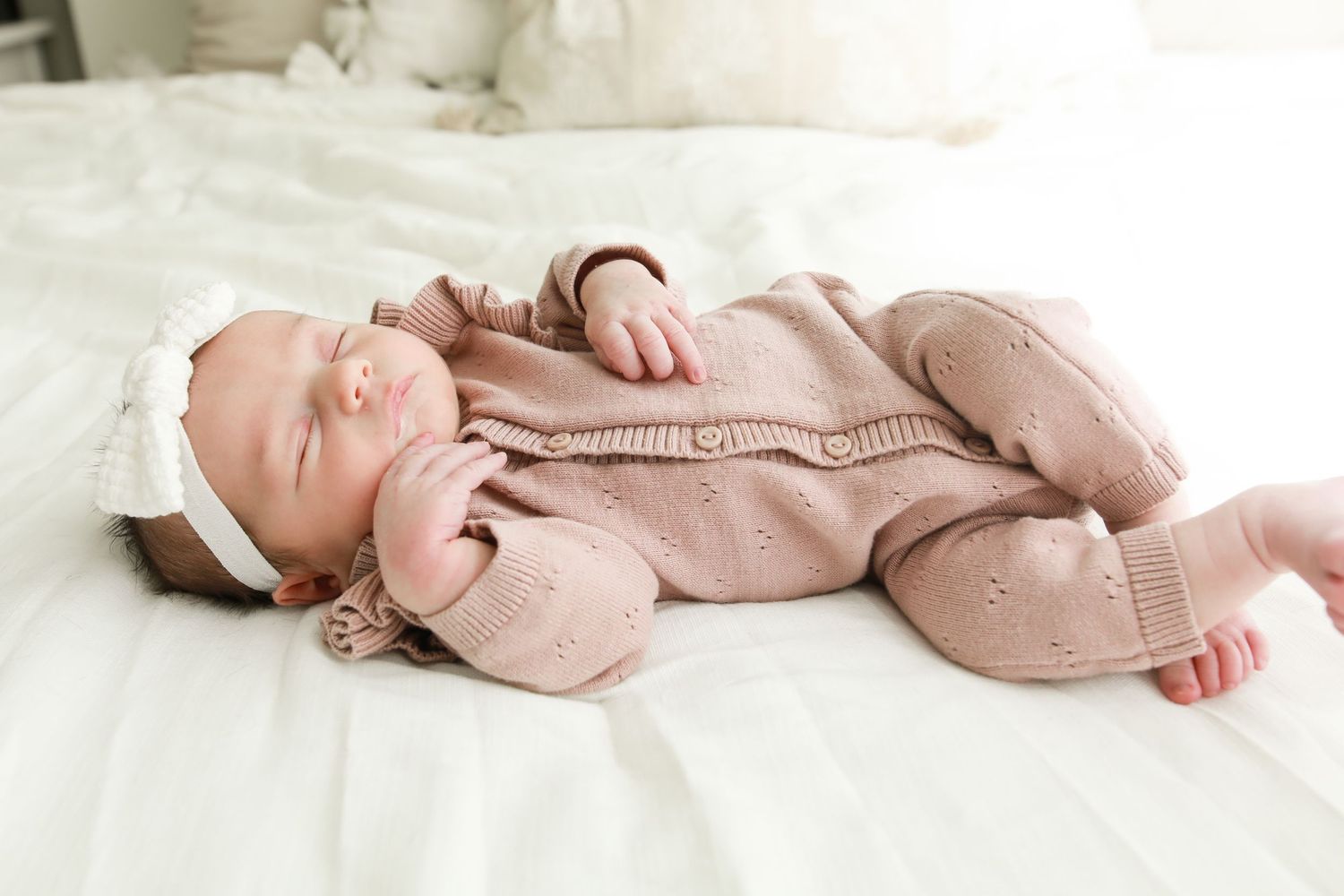 Infant dressed in pink outfit lying on white blanket during newborn photography session.