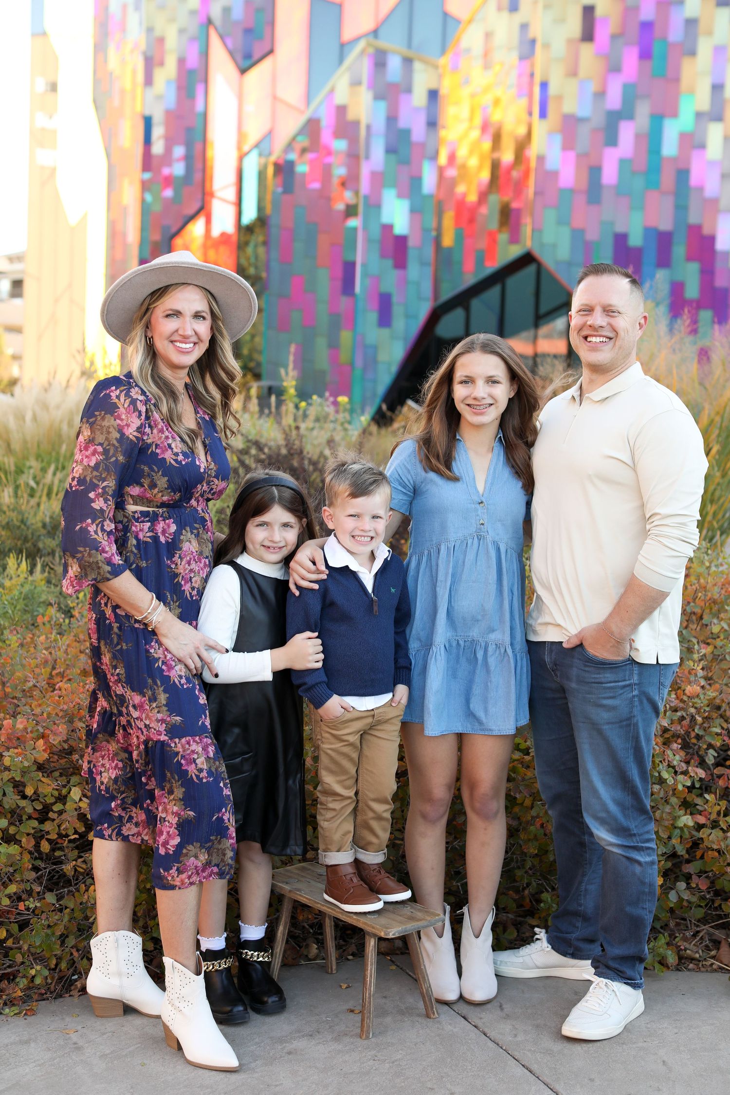 A group poses in front of a colorful geometric mural wall outdoors.