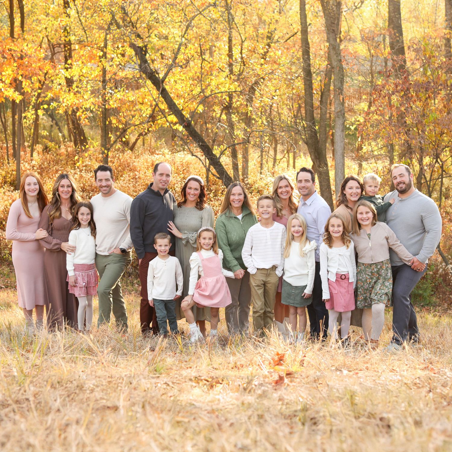 Large multi-generational family portrait in coordinated outfits against autumn foliage.