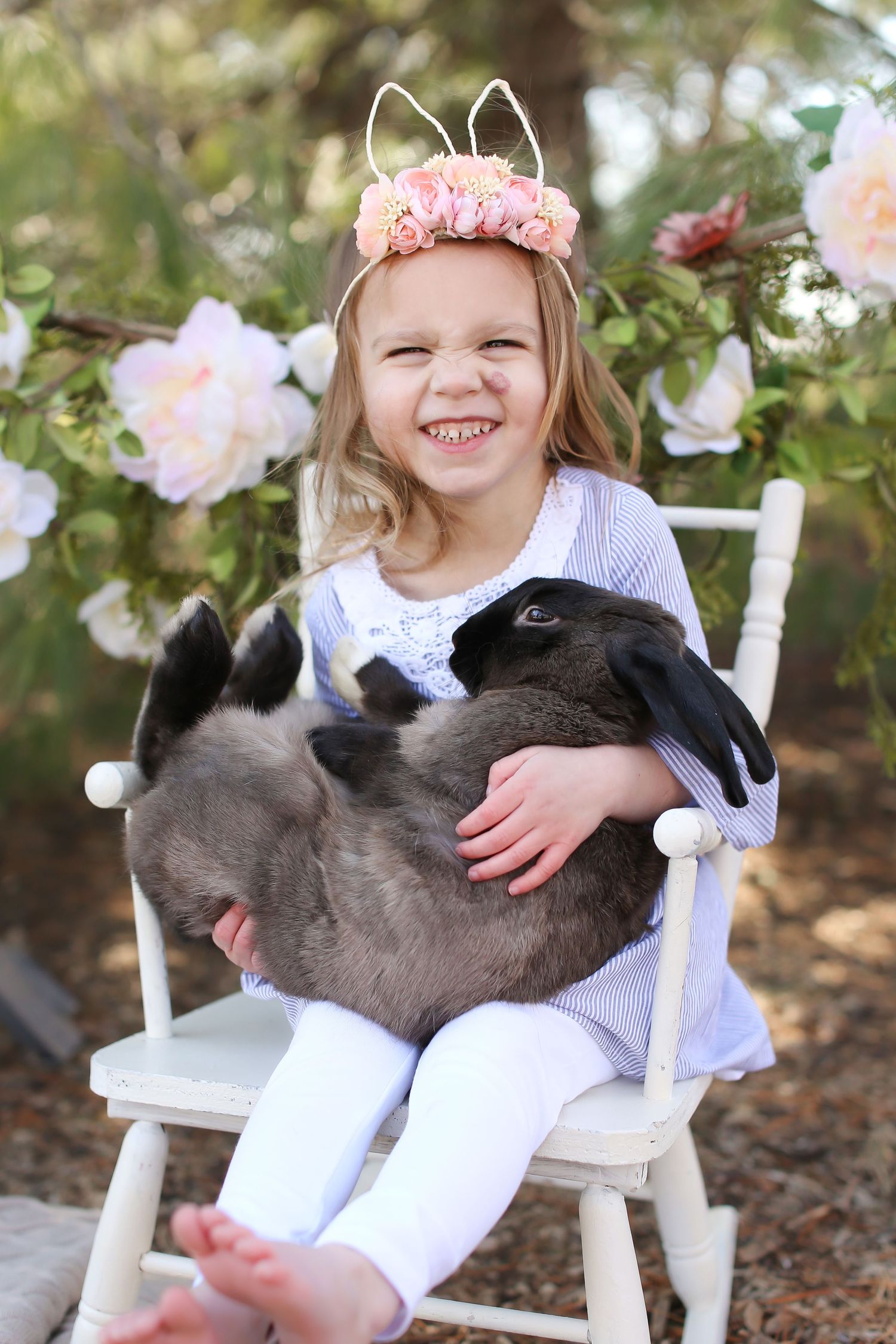 Child sitting in white chair holding a fluffy grey bunny with floral decorations.