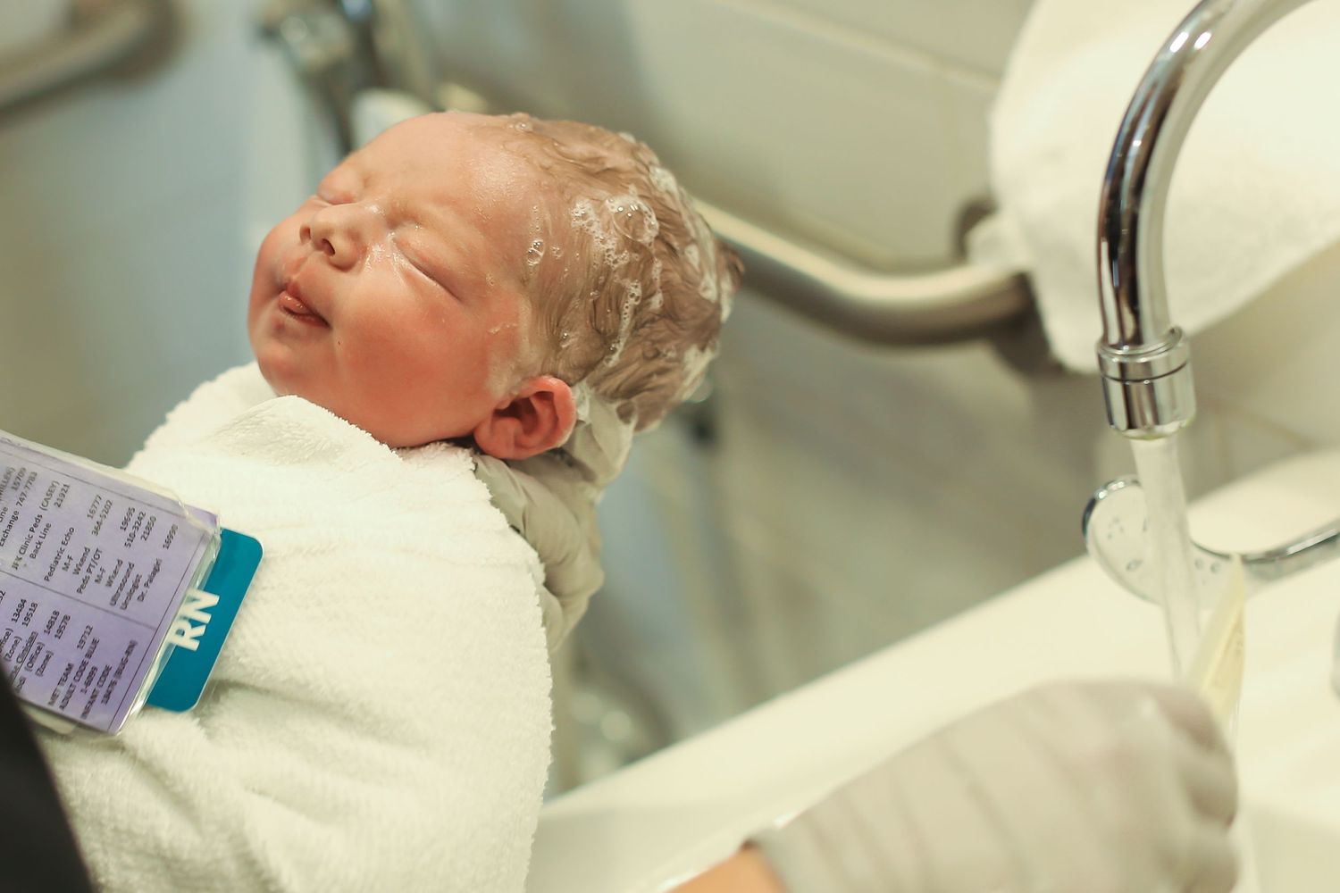Newborn receiving first medical assessment near hospital sink.