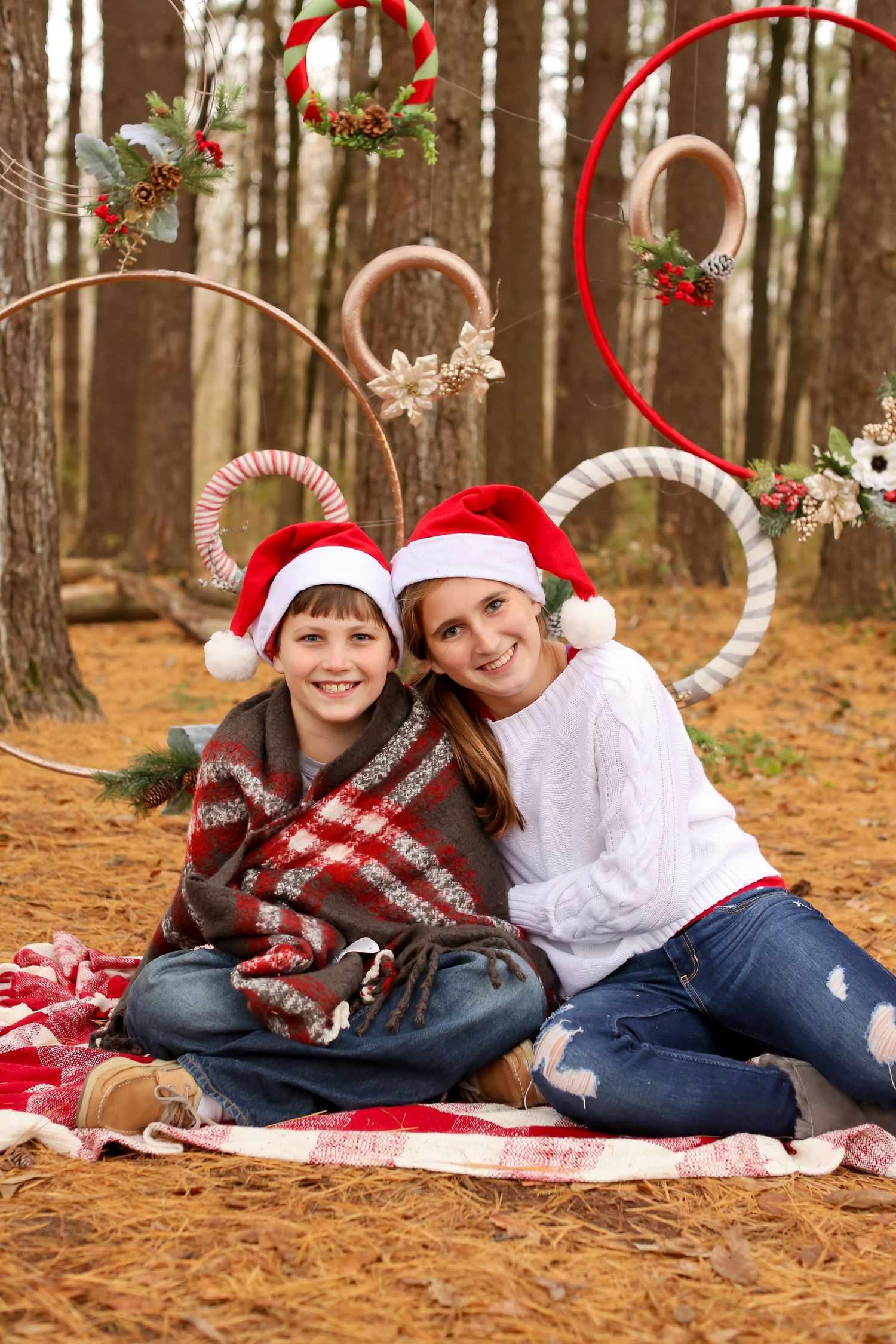 Christmas themed family photo on red plaid blanket with candy cane decorations in forest setting.