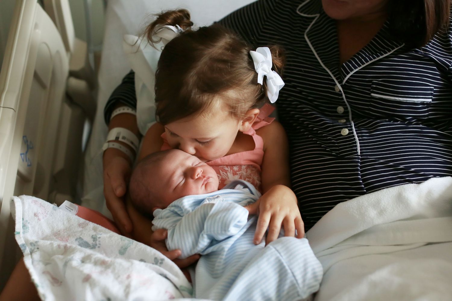 Sibling meeting new baby in hospital room setting.