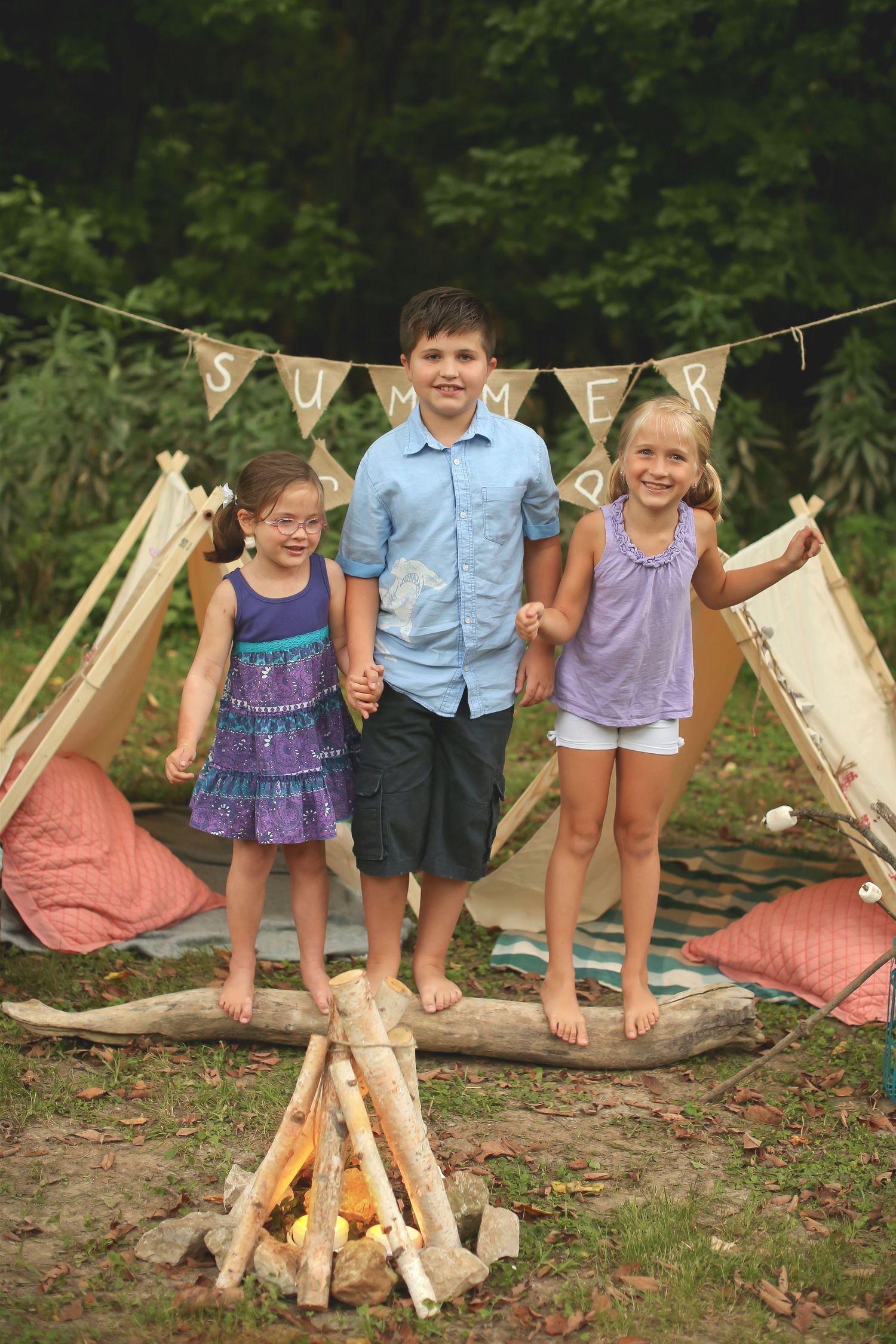 Children enjoying outdoor playtime around a rustic teepee setup with banner decorations.