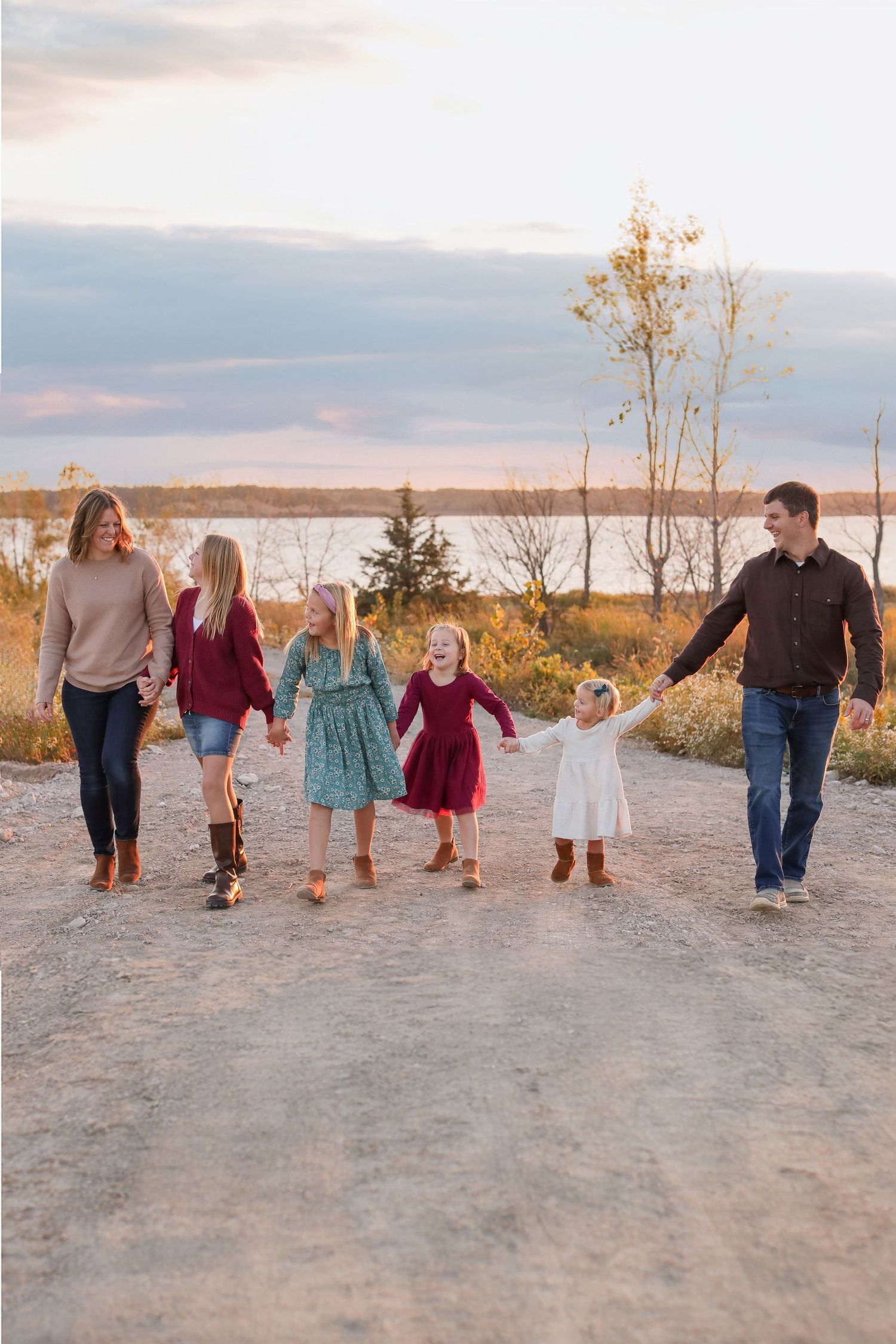 Family walking together on sandy beach path during golden hour sunset.