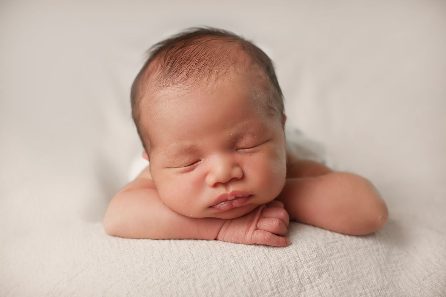 Newborn baby sleeping peacefully in soft white blankets during professional photo session.