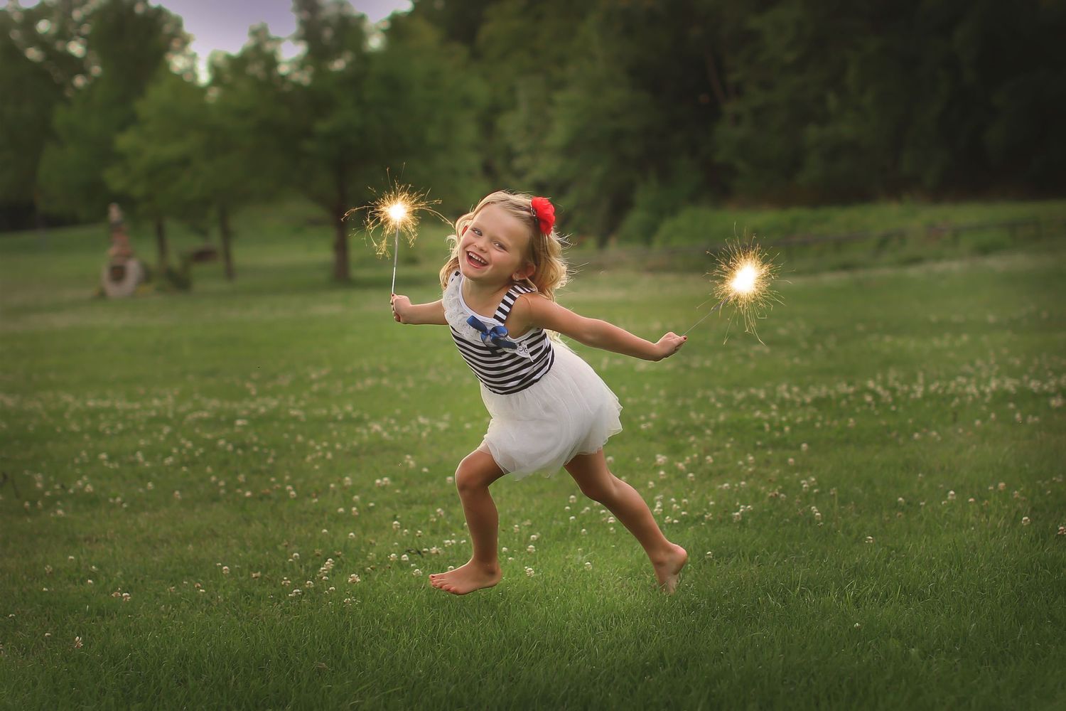 Figure in white dress dances with sparklers at twilight in grassy field.