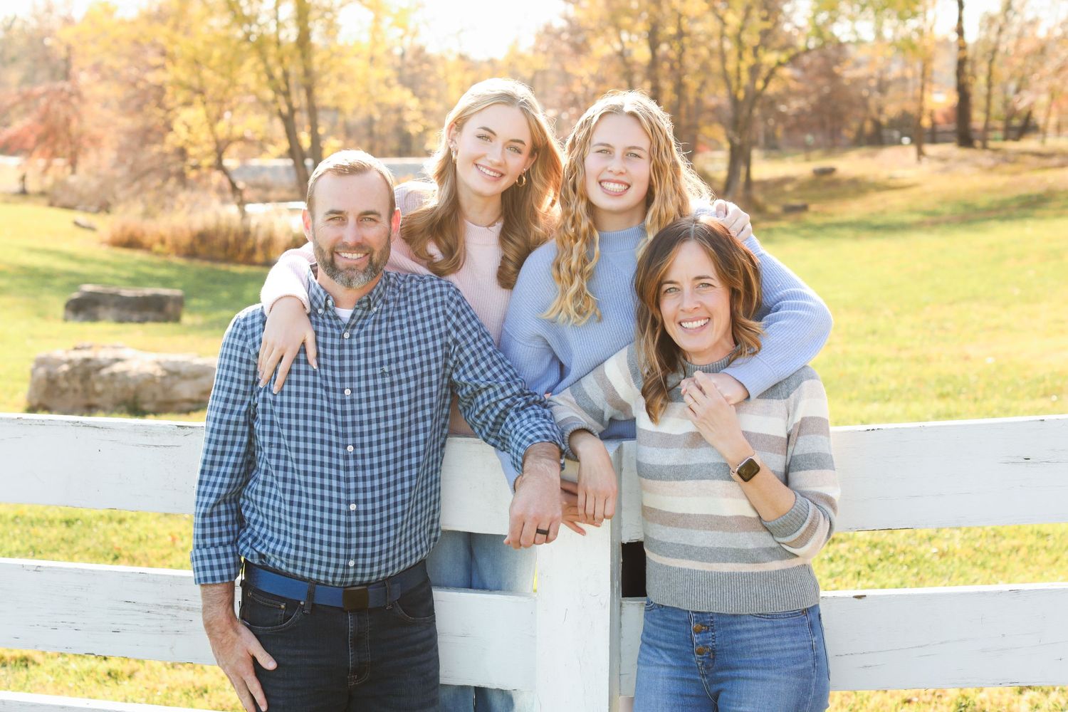 Family posing together by a white fence in an autumn field during golden hour.