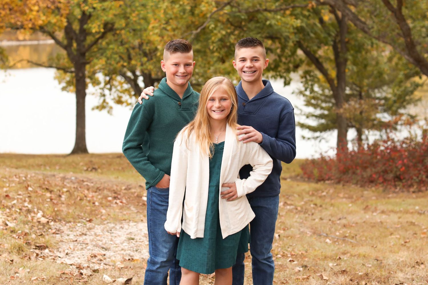 Three people posing outdoors together on a fall day with autumn trees in the background.