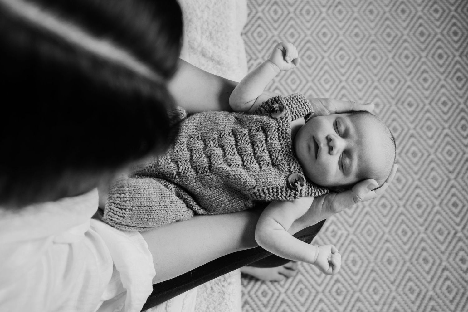 Black and white portrait of a sleeping newborn baby resting peacefully in a parent's arms.
